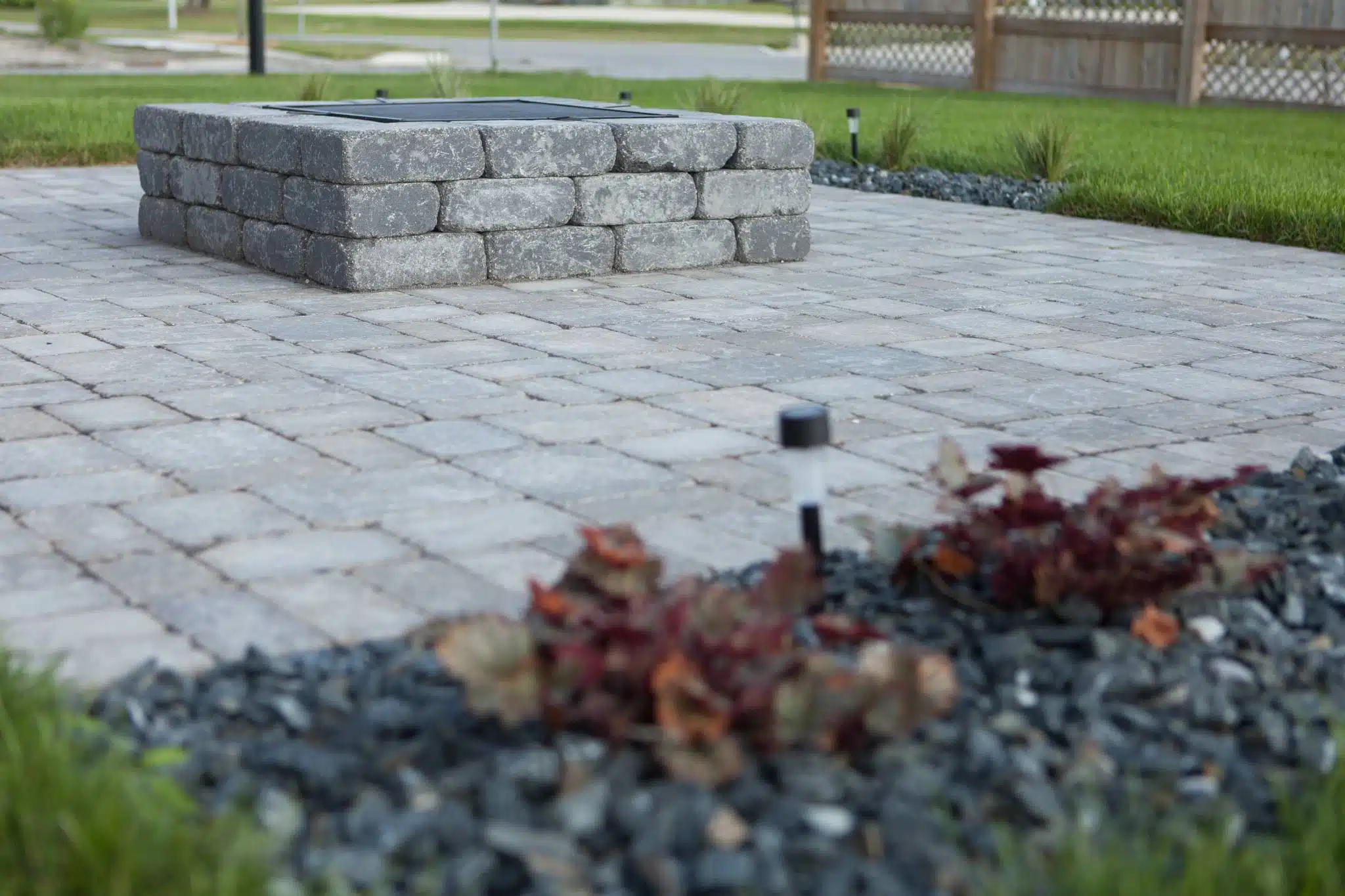 Square stone fire pit on a patio with pavers and landscaping