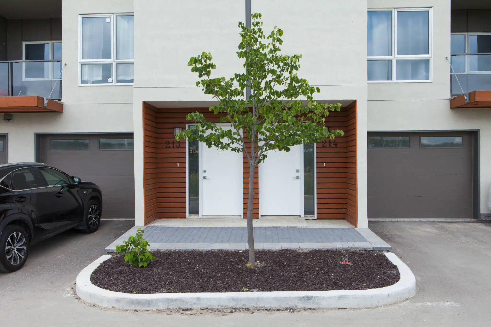 Two modern townhouse entrances (215 & 214) with small tree, driveway, and parked car