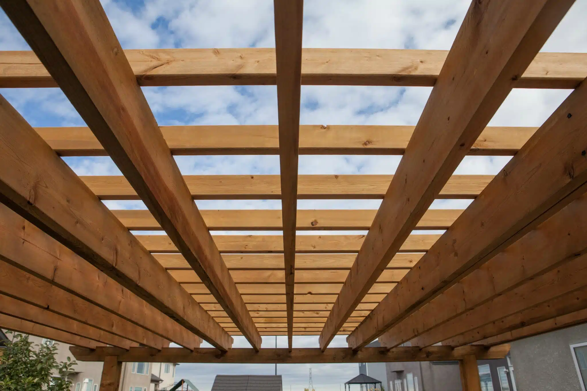 Looking up at a wooden pergola with the blue sky and white clouds in the background