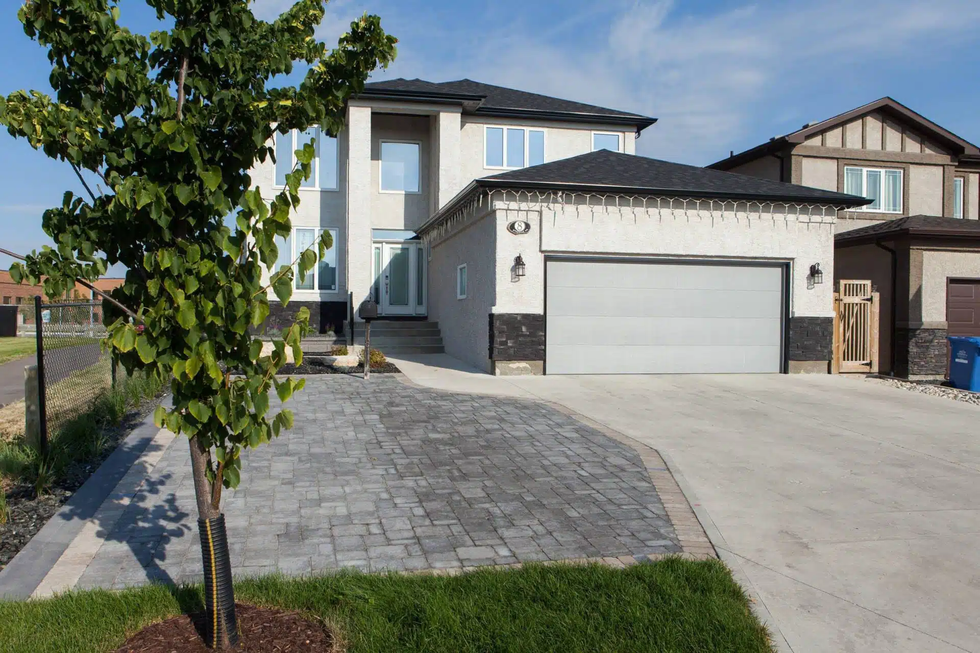 Large driveway, brick patio and planting bed, with suburban home in background.