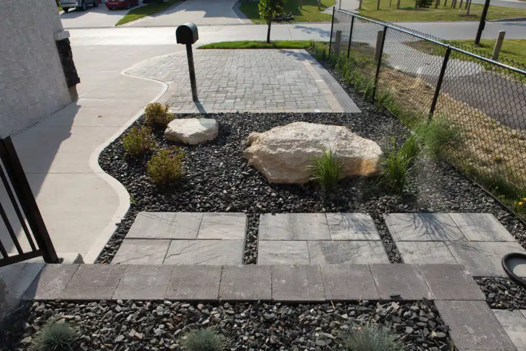 A front yard with a paved driveway, rock garden, and stone pathway