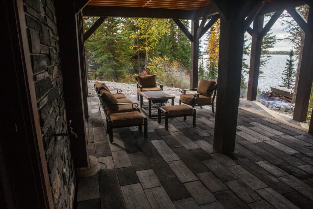 Multi-coloured brick patio, with outdoor furniture, for a cabin property, with fall coloured pine trees in the background over looking a body of water.