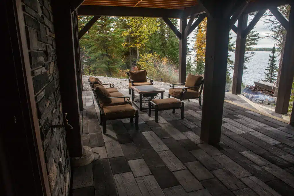 Covered patio with wood-look tile, rustic furniture, overlooking lake and forest