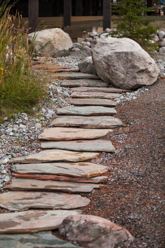 Natural rock slab walkway with large rock features and stone planter beds on either side for a cabin property.