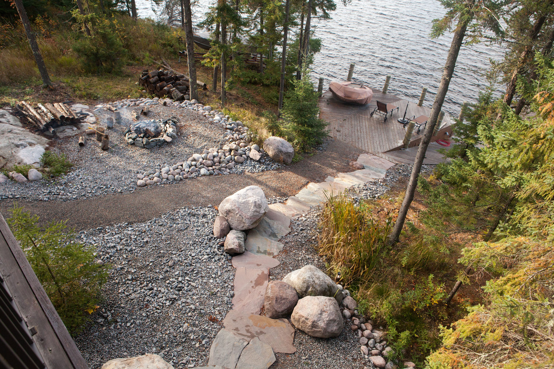 Landscaped gravel and rock pathway for a cabin, overlooking a dock and water.