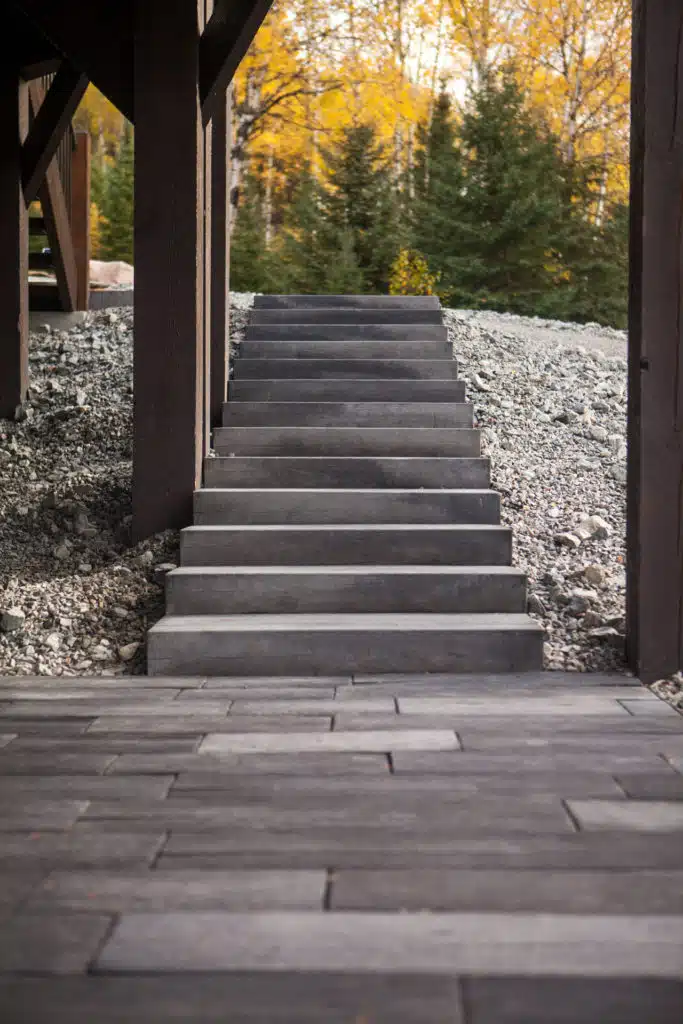 A set of grey stone steps leading up from a wood deck, with trees in the background