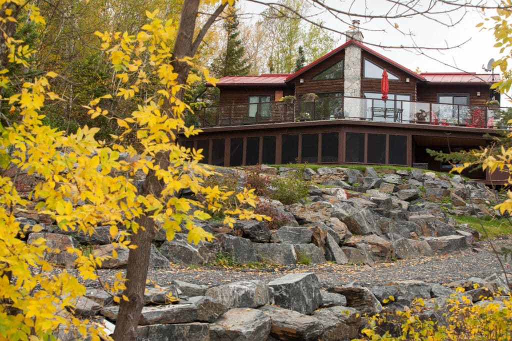 Stone retaining walls in front of cabin with red roof and fall coloured trees.