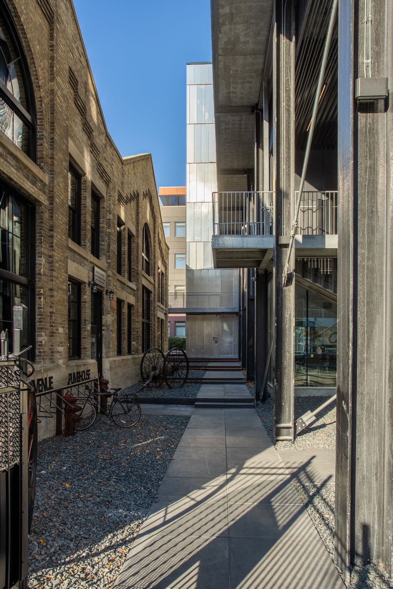 A designer build downtown alley pathway, between a brick business building and brick residential condos, with sleek concrete slate steps and gravel.