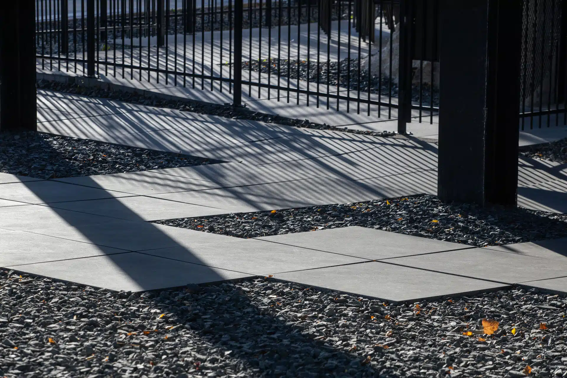 Paved stone path through gravel landscaping next to black metal fence