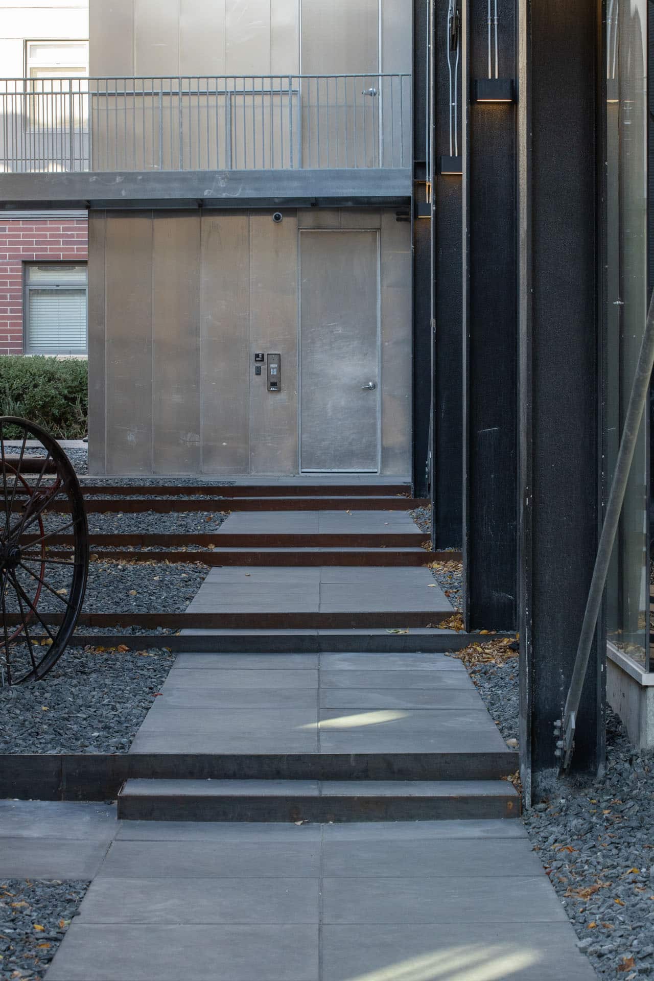 A detail of a modern landscaped downtown alley pathway, between a business building and residential condos, with concrete slate steps and gravel.