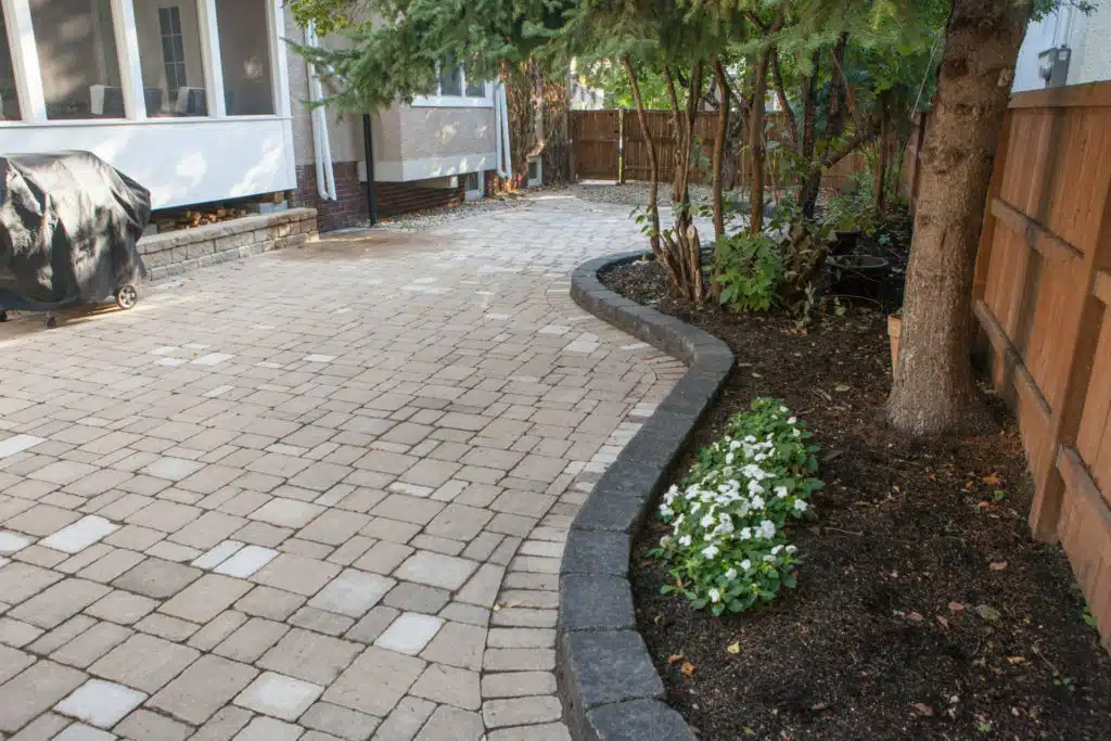 Patio with light-colored pavers, black edging, and flower bed