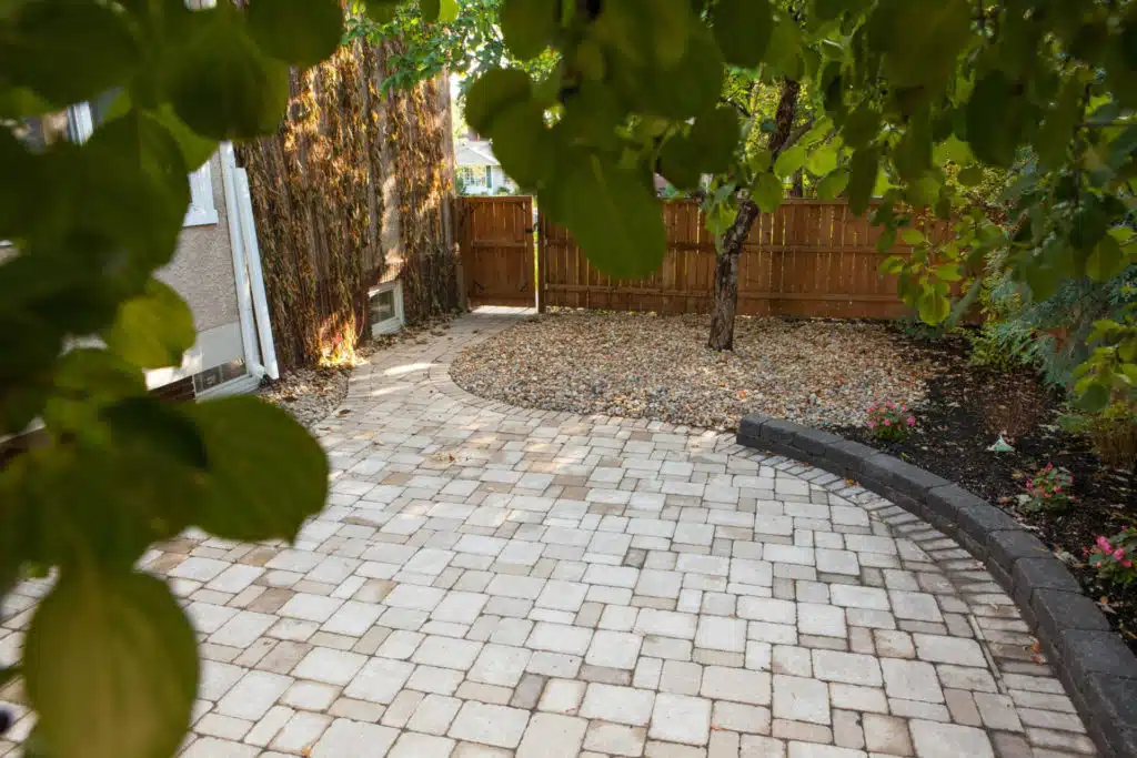 Backyard patio with light-colored pavers, gravel border, and gate in wood fence