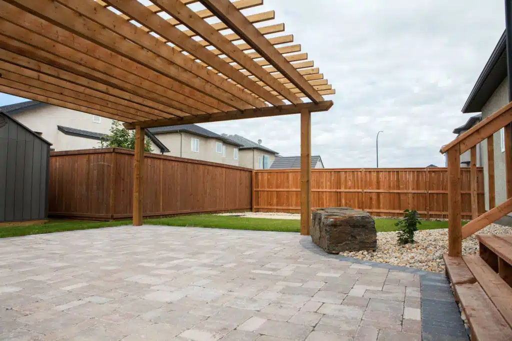 A backyard with a wooden pergola over a stone patio