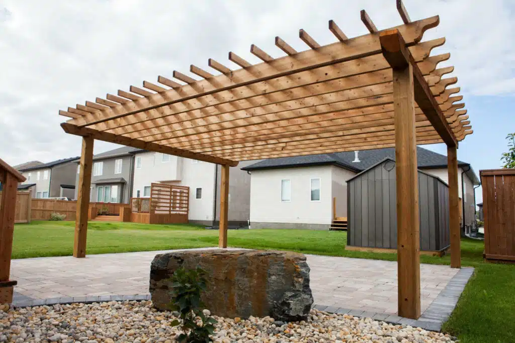 A large wooden pergola stands in a backyard on a stone patio