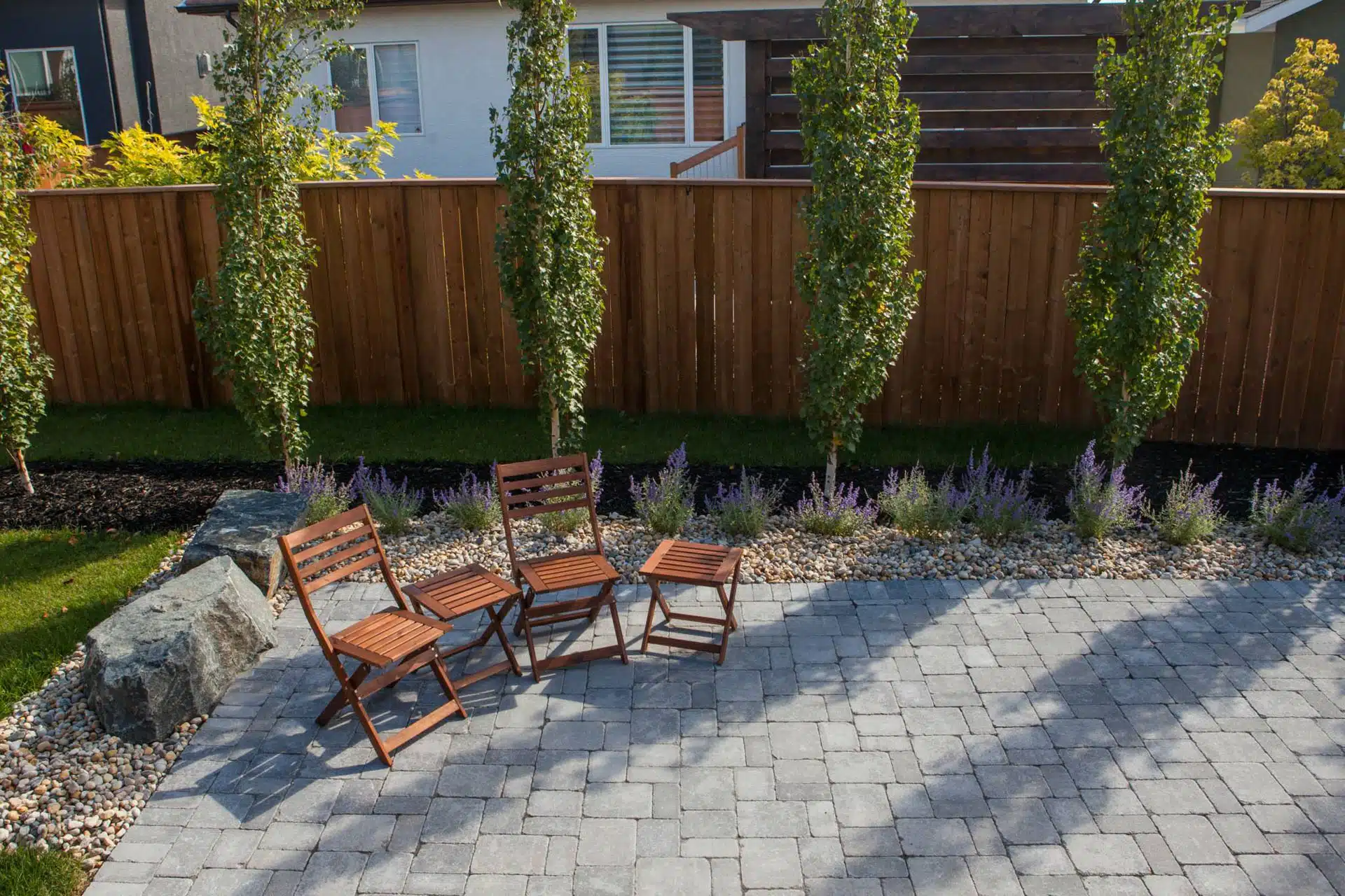 Wooden fence and outdoor furniture with rock planting bed and landscaping.