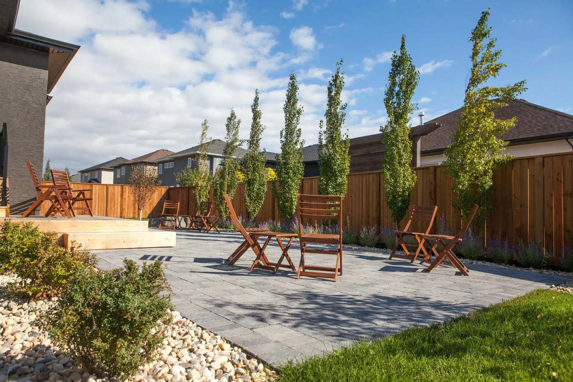 Wooden fence, deck and outdoor furniture, with rock planting bed in Winnipeg backyard.