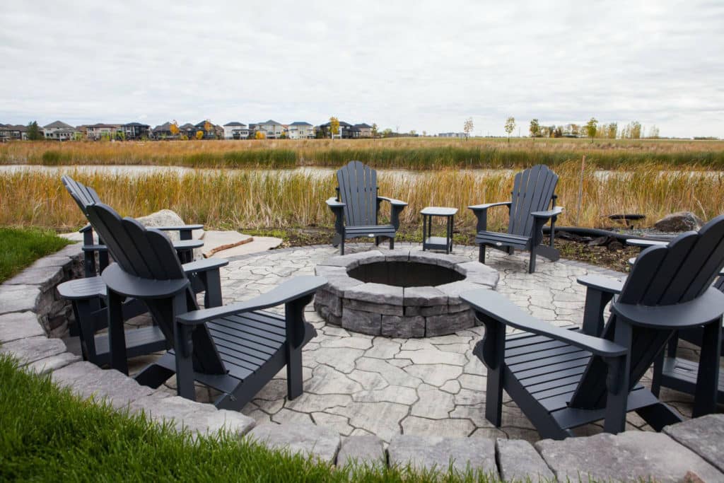 Circular stone patio and fire pit with retainer wall and outdoor furniture overlooking grasslands.