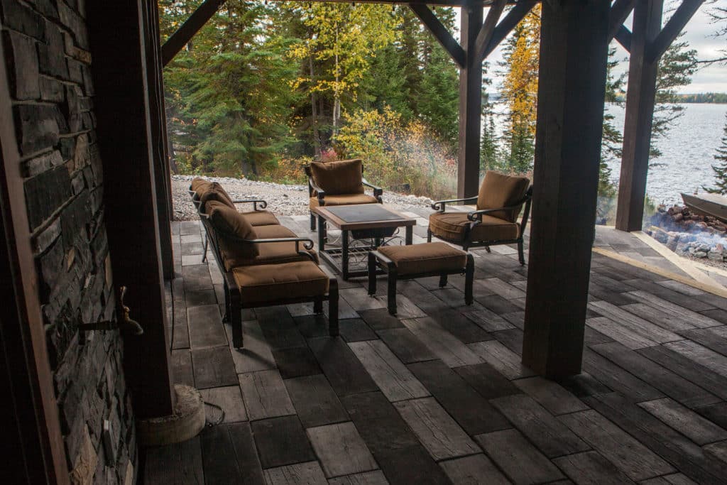 Stone patio at the cabin with outdoor table and chairs. Fall coloured trees and a lake in the background.