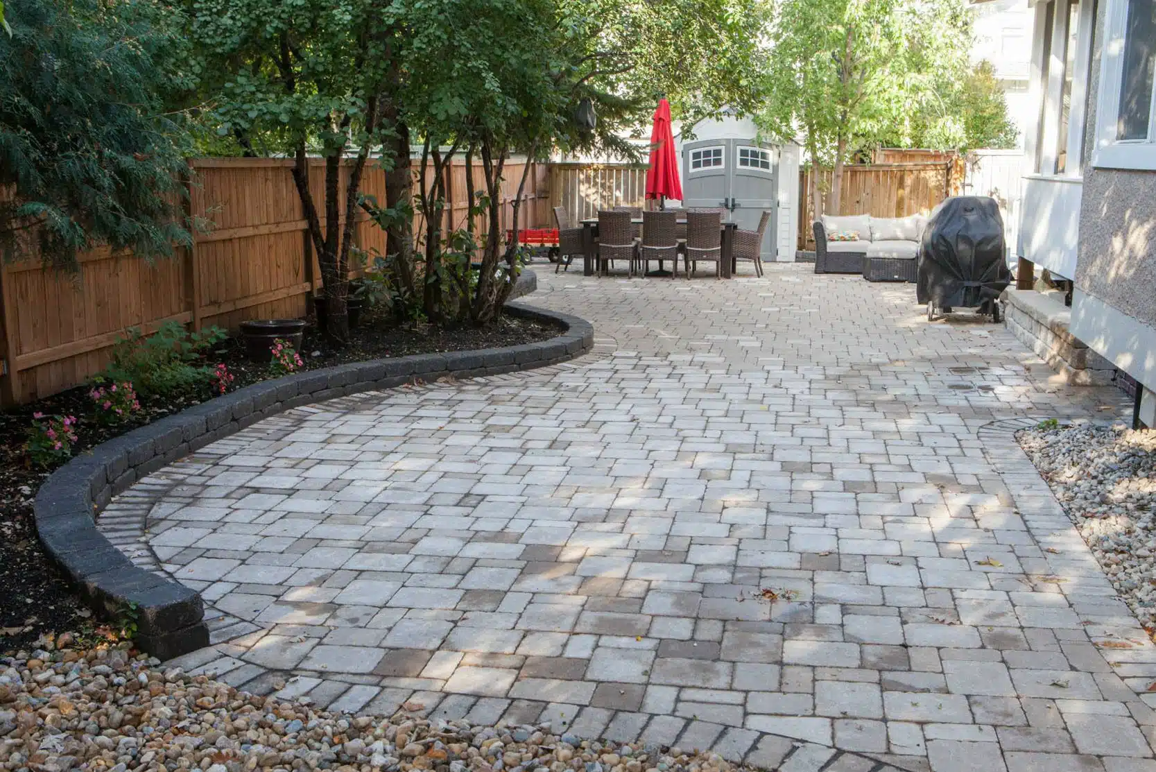 Backyard patio with stone pavers, a curved retaining wall, and a dining area