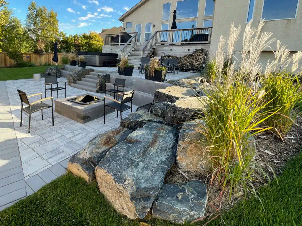 Backyard patio with fire pit, hot tub, stone wall, and ornamental grasses
