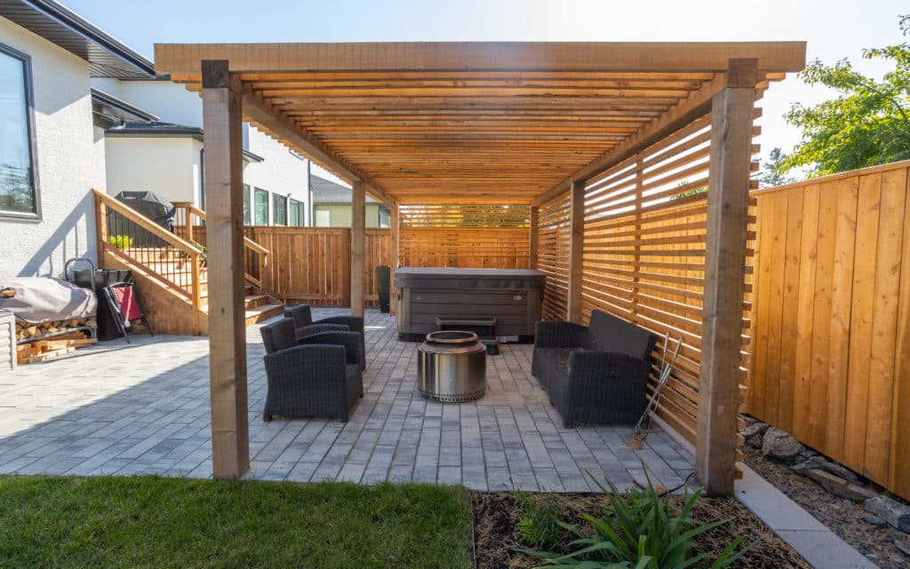 Beautiful wooden pergolas above stone patio and fire pit, surrounded by modern fence.