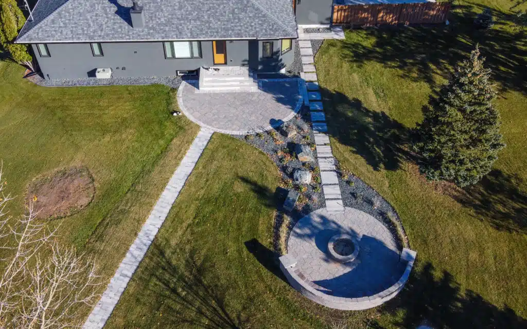 Aerial view of a backyard with a paved patio, fire pit, and stone walkways