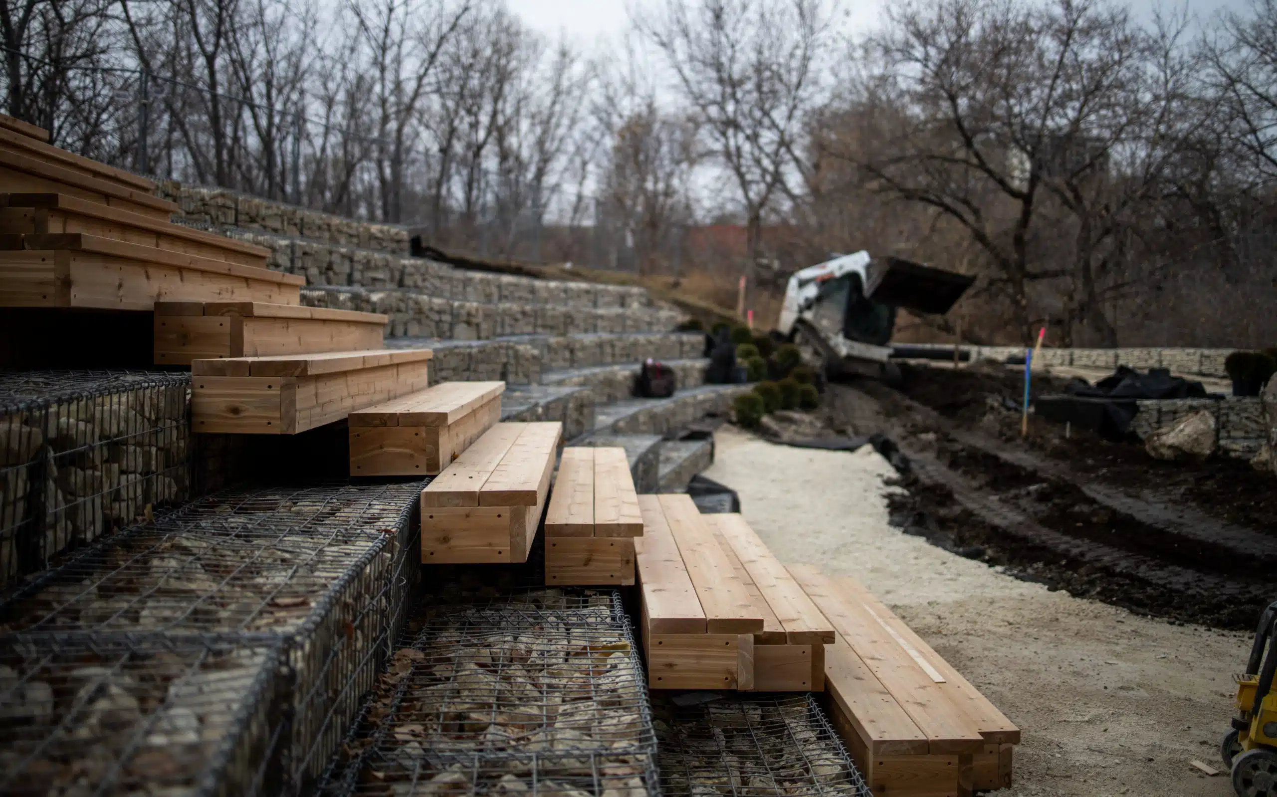 Outdoor amphitheater under construction with wood benches and stone retaining walls