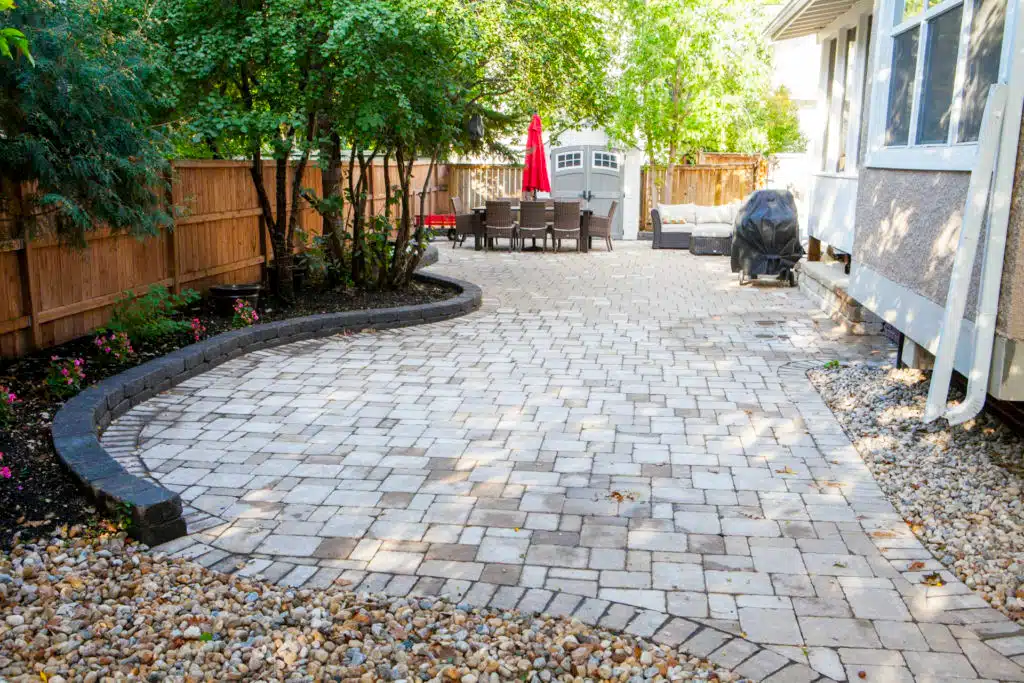 Winnipeg backyard stone patio with flower bed and an outdoor table and chair set.