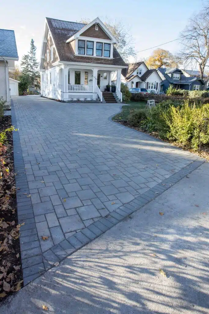 A brick driveway with a grey border leads to a house with a porch