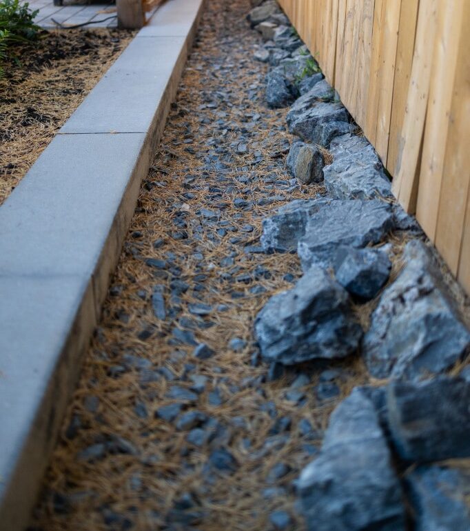 Wooden fence and privacy screen, on either side of a rock planting bed alley.