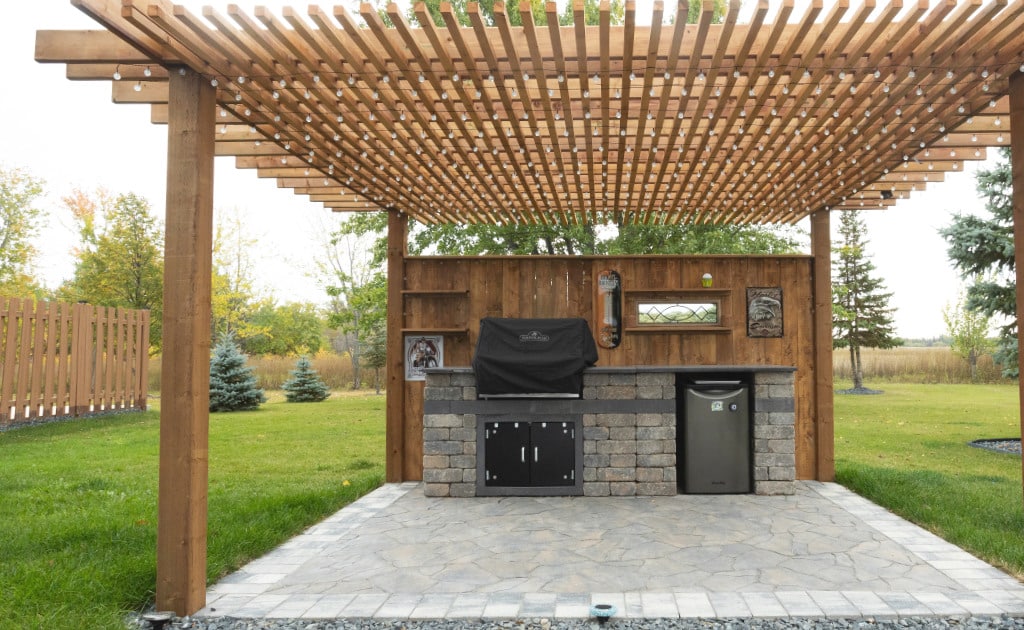 A wooden pergola built over an outdoor kitchen and a stone patio.