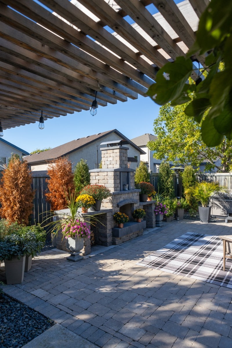 Stone outdoor fireplace beside a pergola.