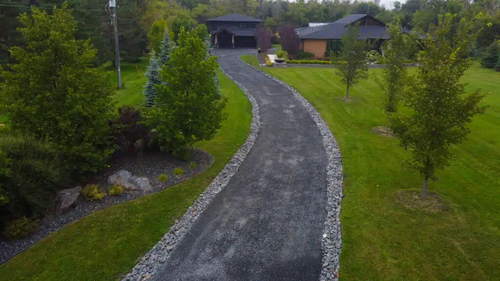 Curved black gravel driveway lined with trees leading to a modern house.