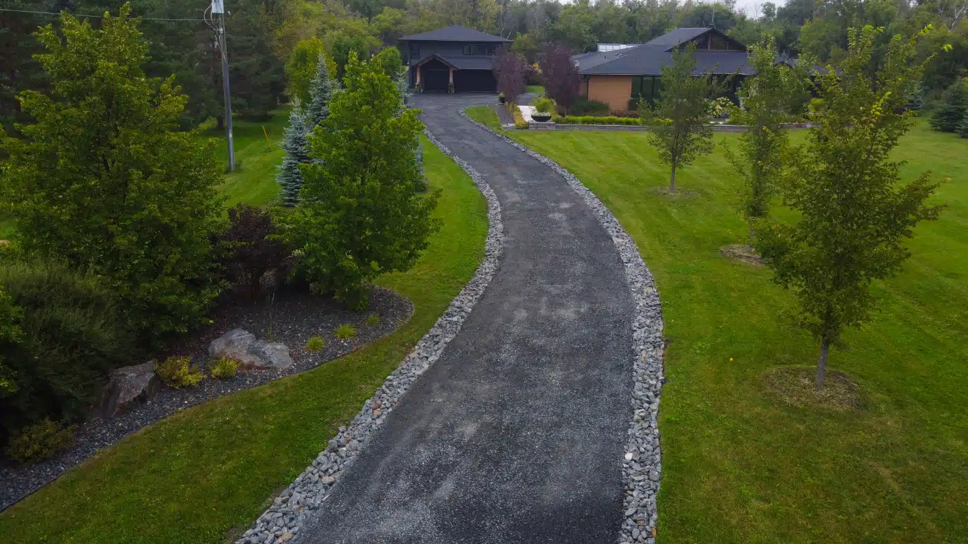 Curved black gravel driveway lined with trees leading to a modern house.