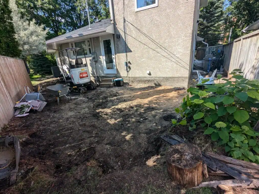Backyard under excavation with dirt ground, wheelbarrows, and a small Bobcat loader.