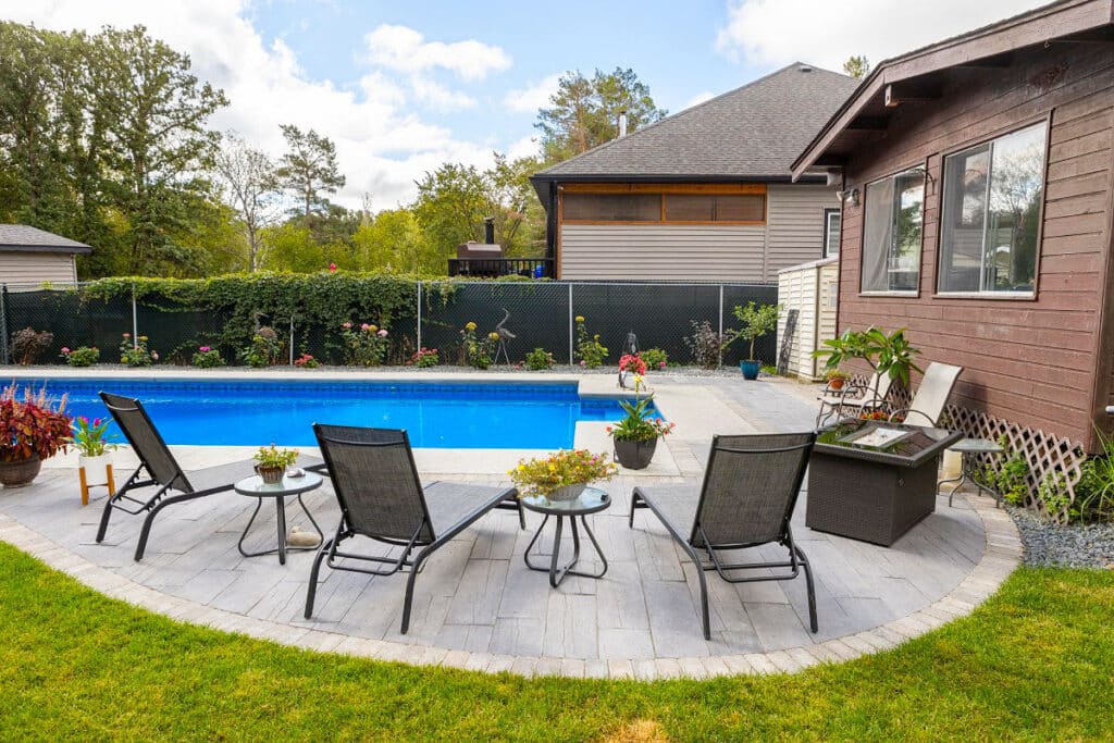 Backyard pool, with surrounding stone patio, rock garden and outdoor furniture.