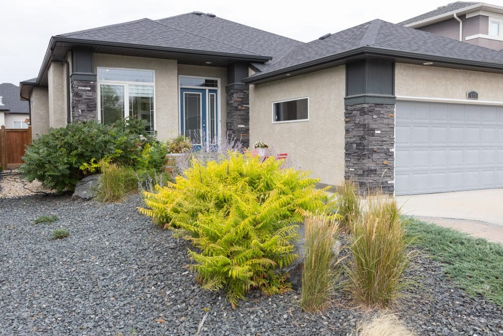 Front yard with decorative stone landscaping, shrubs, and grasses in front of a modern house.