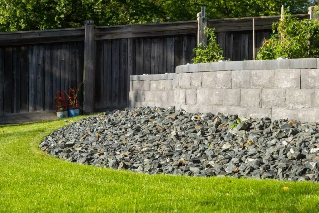 Raised stone retaining wall with decorative rock bed and lawn.