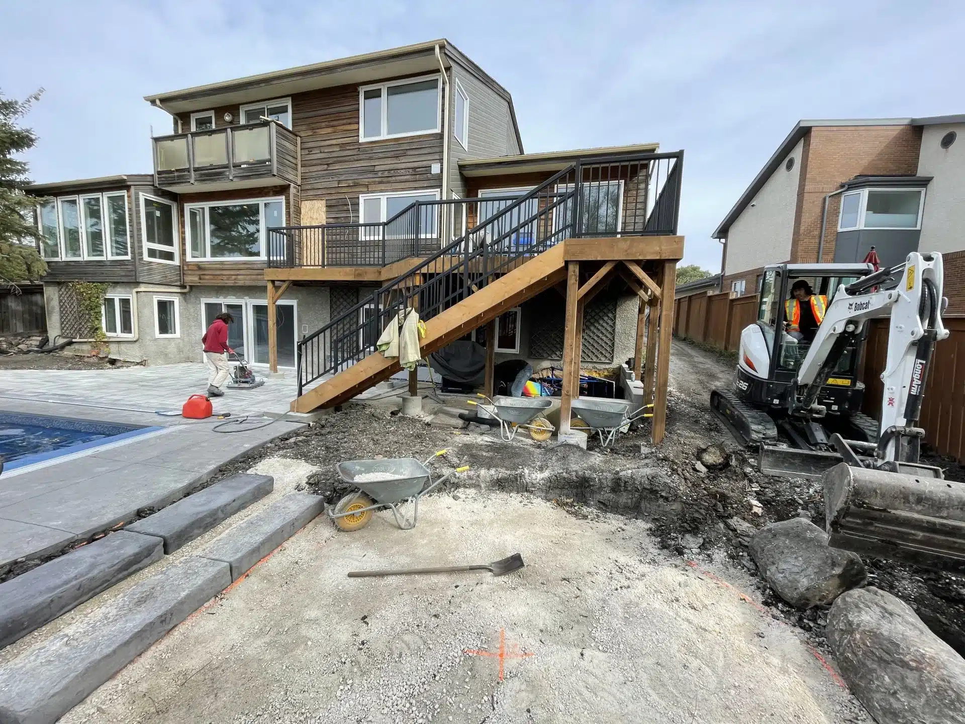 Backyard during landscaping construction with deck, pool, and equipment.