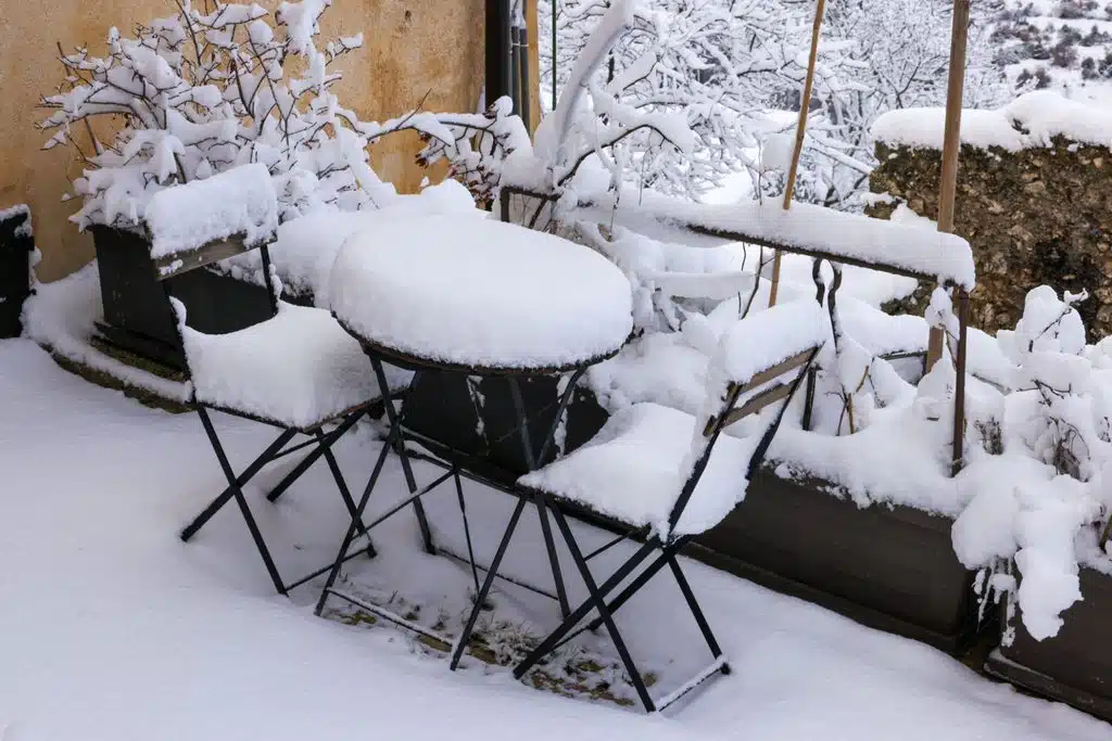 Outdoor patio table, chairs and planters covered in heavy snow during winter.